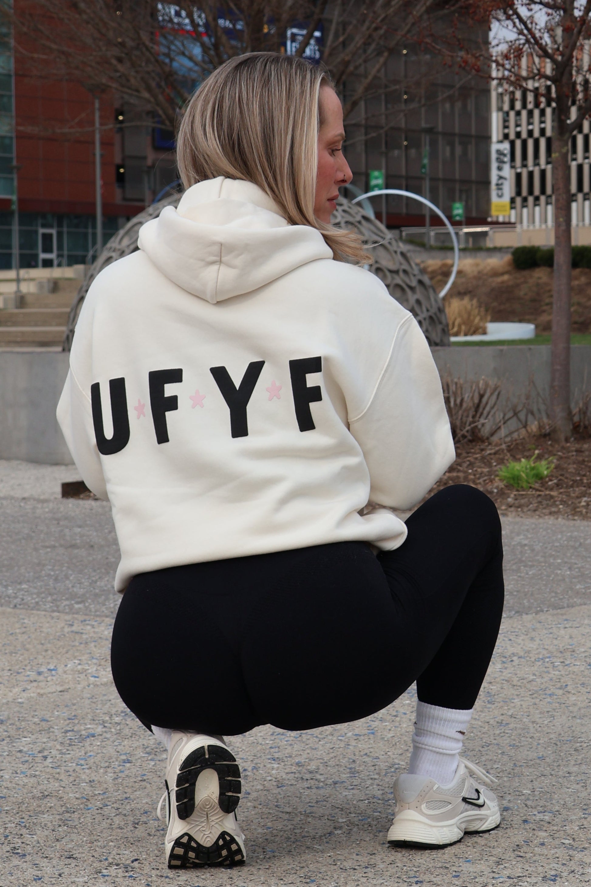 Person wearing a hoodie with 'UFY' on it, standing on a street with buildings in the background.