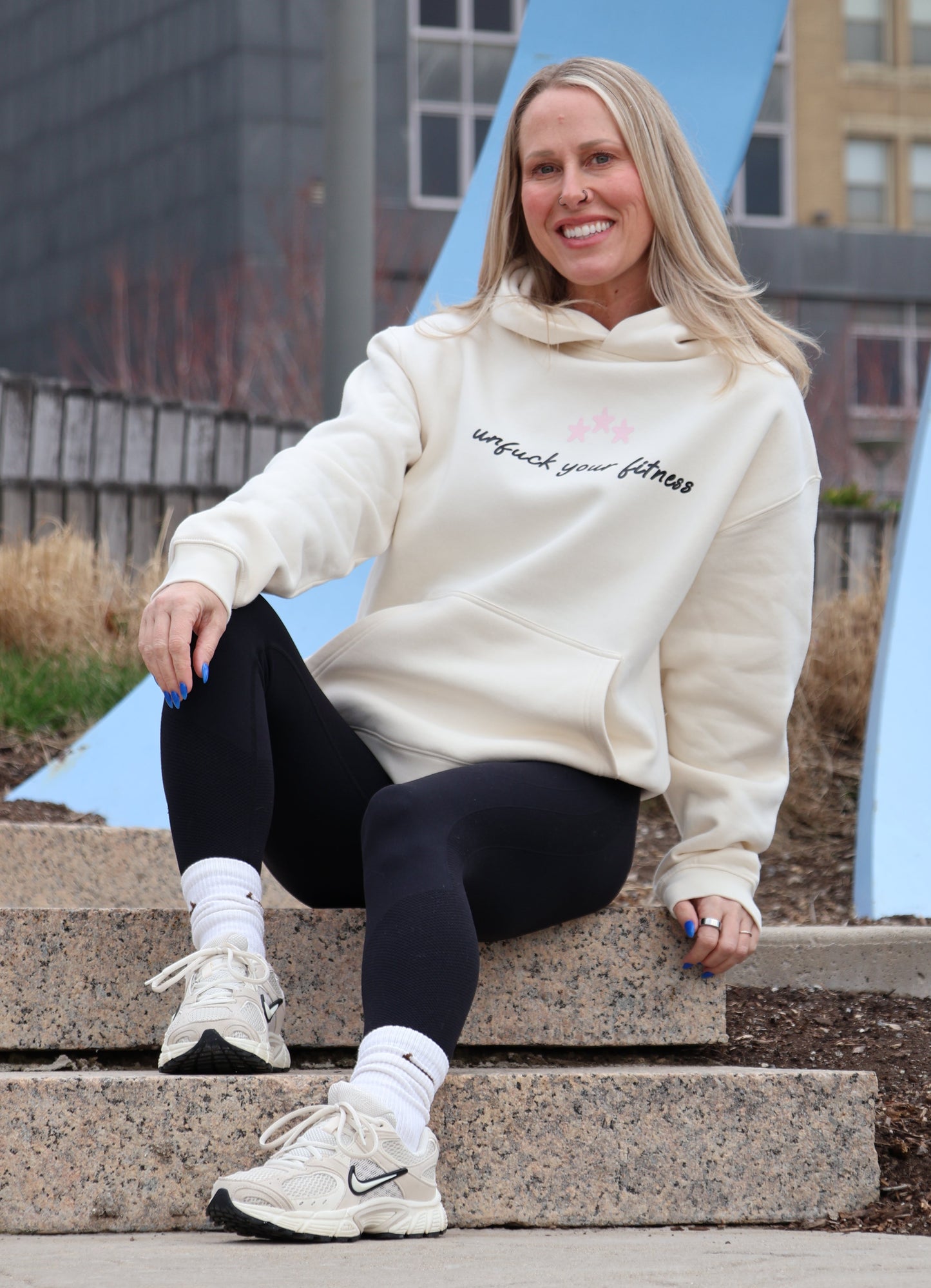 Person wearing a white hoodie with text, black pants, and white sneakers on a city street.