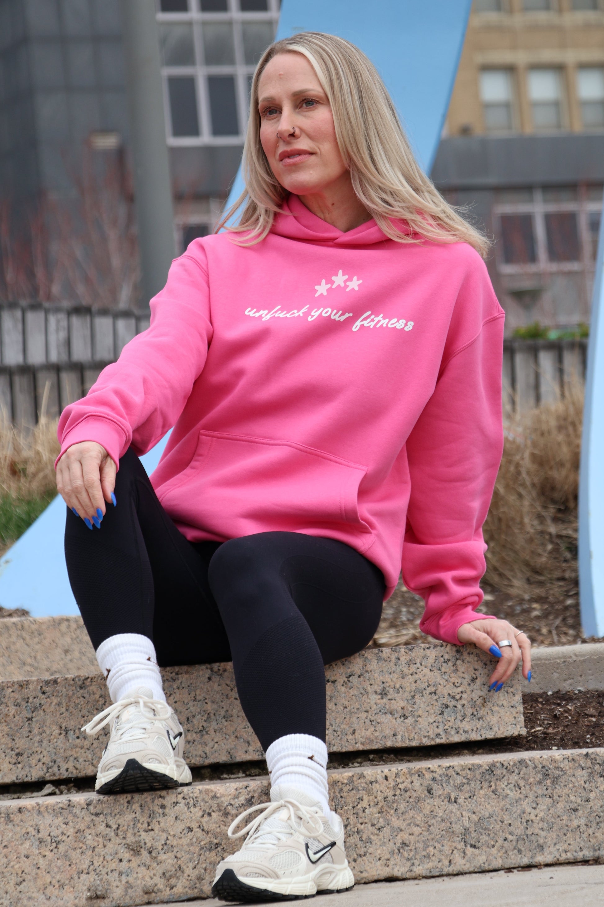 Person wearing a pink hoodie with text, sitting on steps outdoors.