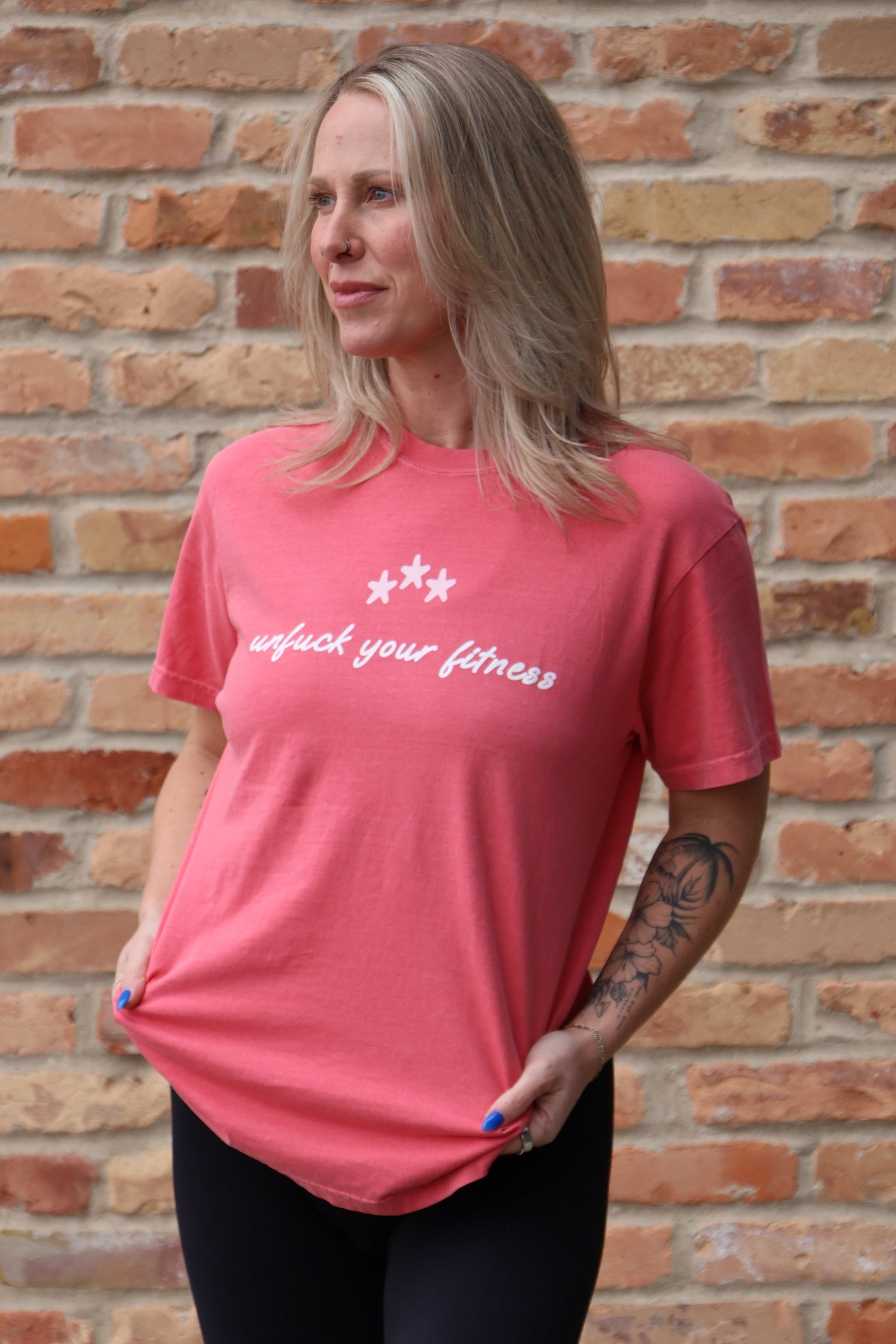Person wearing a pink shirt with text in front of a brick wall
